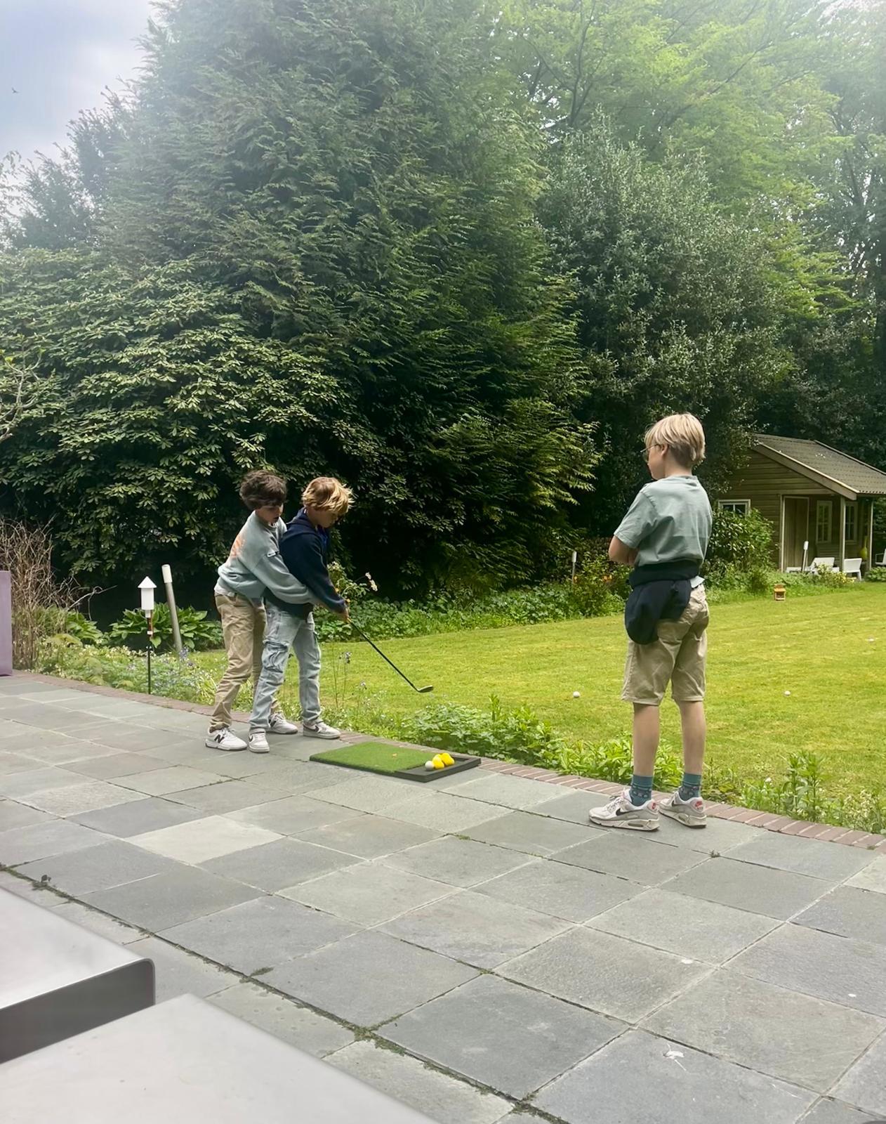 Nathan geeft zijn schoolvriendjes een gratis golfles op de oefenmat in de achtertuin