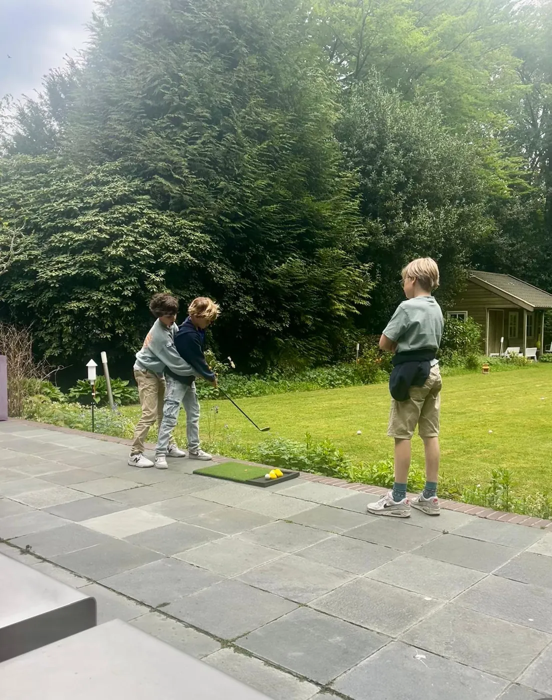 Nathan geeft zijn schoolvriendjes een gratis golfles op de oefenmat in de achtertuin