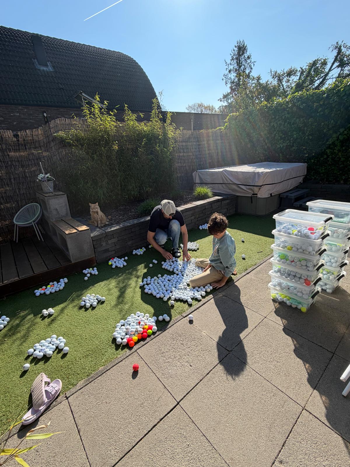 David en Nathan maken honderden gevonden golfballen schoon en sorteren ze in de achtertuin, met de voorraadboxen op stapel